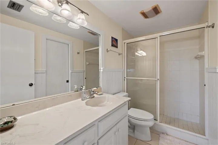 Full bathroom with vanity, a wainscoted wall, a stall shower, and light tile patterned floors