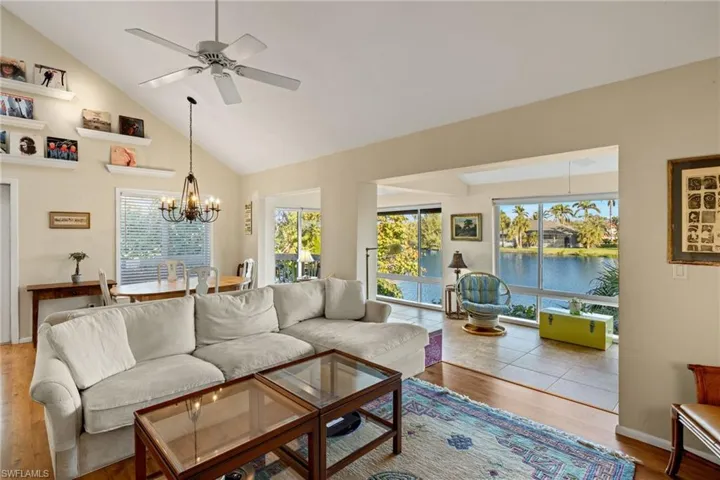 Living room with high vaulted ceiling, a water view, a chandelier, wood finished floors, and ceiling fan