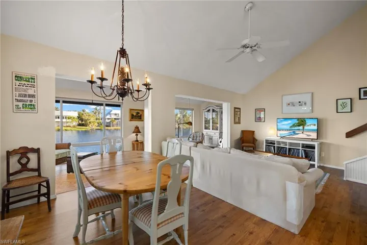 Dining space featuring high vaulted ceiling, wood finished floors, ceiling fan, a chandelier, and a water view
