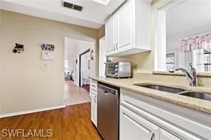 Kitchen with appliances with stainless steel finishes, white cabinetry, light wood-style flooring, under cabinet range hood, and light stone countertops