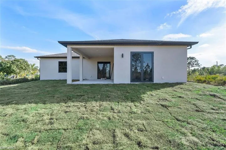 Back of house with stucco siding, a yard, a patio, and french doors