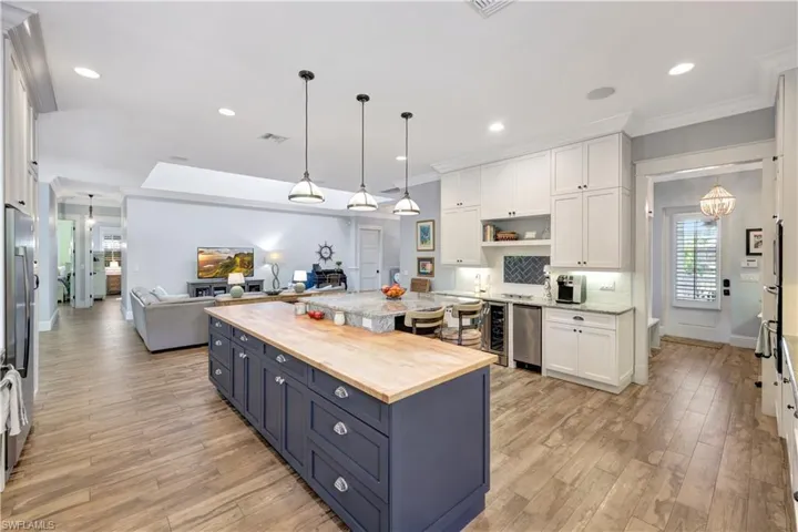 Kitchen featuring butcher block countertops, decorative light fixtures, white cabinetry, open floor plan, and a kitchen island