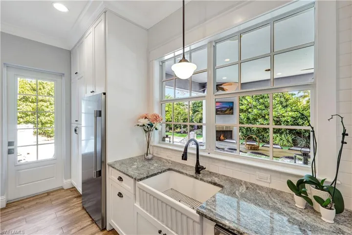 Kitchen with light stone counters, white cabinetry, farmhouse style sink, decorative light fixtures, and crown molding