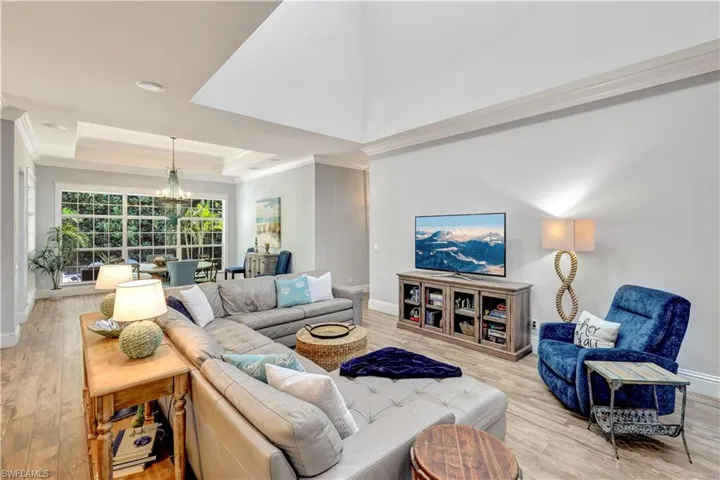 Living room with a tray ceiling, light wood-type flooring, a chandelier, and crown molding