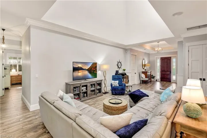 Living room with a chandelier, crown molding, light wood- flooring, and a tray ceiling