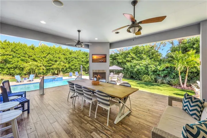 Open porch with outdoor dining space, a warm lit fireplace, a pool with connected hot tub, a patio area, and a ceiling fan