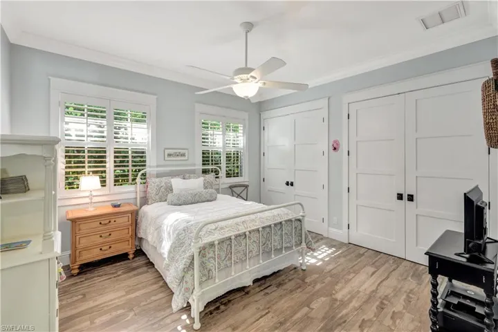 Bedroom featuring ornamental molding, multiple closets, light wood-type flooring, and ceiling fan