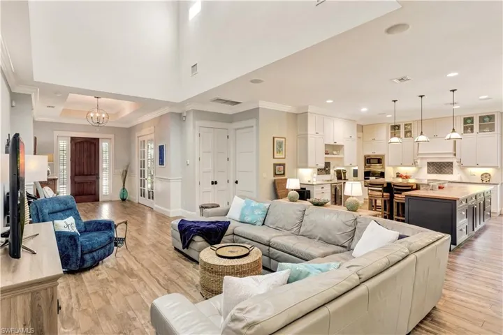 Living room with ornamental molding, light wood-style flooring, a tray ceiling, beverage cooler, and a chandelier