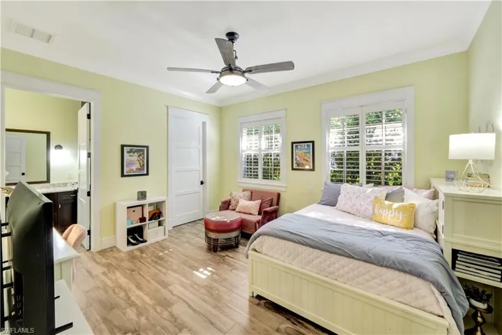 Bedroom featuring ornamental molding, light wood-type flooring, ceiling fan, and ensuite bath