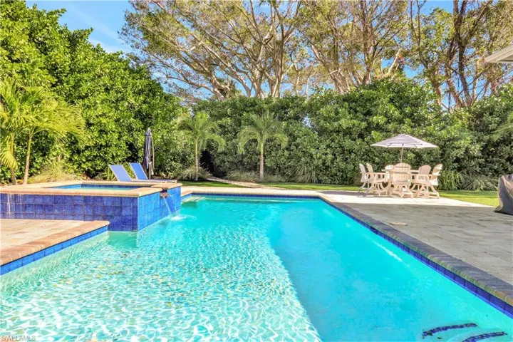 View of swimming pool featuring a patio, a pool with connected hot tub, and view of scattered trees