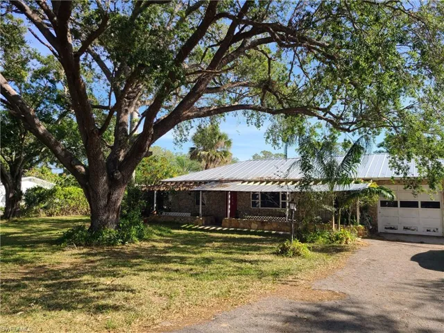 Ranch-style house with a garage, dirt driveway, a front yard, and metal roof