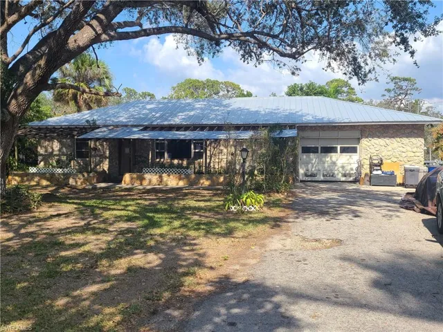 View of front of house with a garage, stone siding, driveway, and metal roof