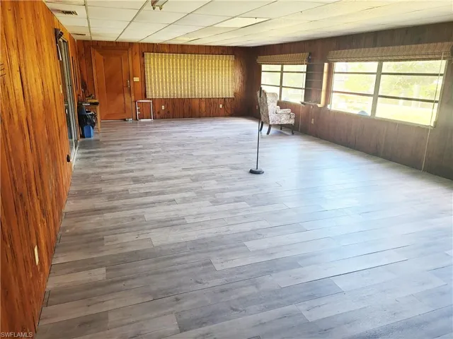 Empty room with a paneled ceiling, visible vents, wooden walls, and vinyl finished floors