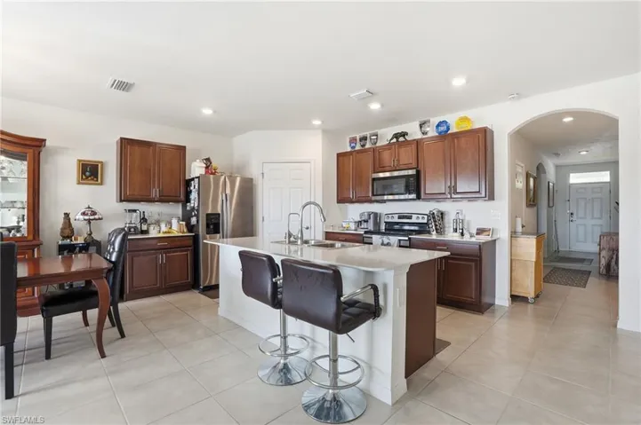 Kitchen with arched walkways, a breakfast bar area, stainless steel appliances, a center island with sink, and light tile patterned flooring
