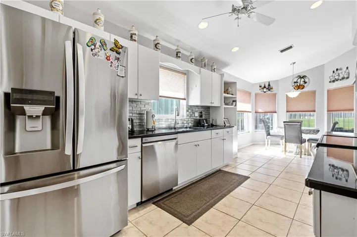 Kitchen featuring stainless steel appliances, decorative light fixtures, white cabinets, backsplash, and light tile patterned floors