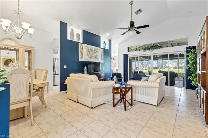 Living room with high vaulted ceiling, light tile patterned flooring, ceiling fan, and a chandelier