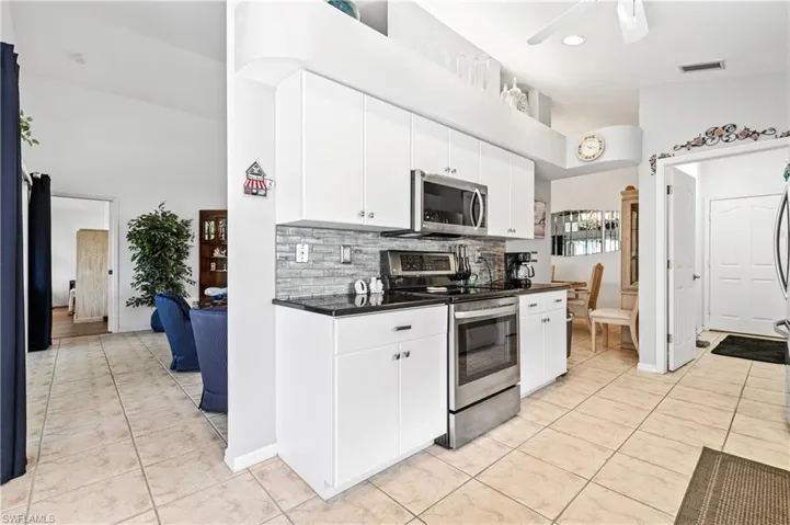 Kitchen featuring stainless steel appliances, decorative backsplash, light tile patterned floors, white cabinets, and a ceiling fan