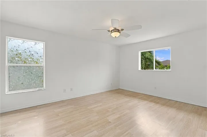 Light wood-finish flooring, white walls, two windows, and a ceiling fan with integrated lighting