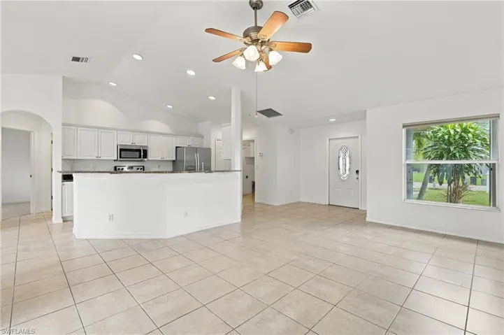 Open concept living area featuring tile flooring, vaulted ceilings, recessed lighting, and a kitchen with white cabinetry and stainless steel appliances