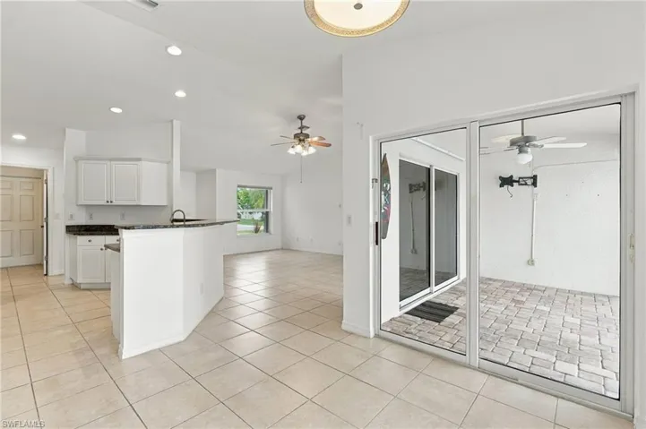 Tile flooring throughout, white cabinetry, dark countertops, built-in breakfast bar, and sliding glass doors to a paved patio