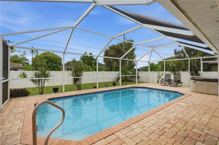 Screened pool enclosure featuring a rectangular pool, brick paver decking, and a built-in hot tub