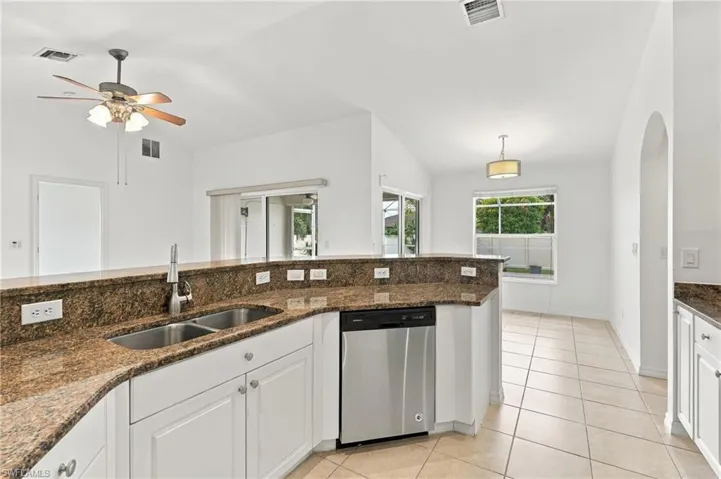 Kitchen featuring a stainless steel double basin sink, white cabinetry, brown granite countertops, and a stainless steel dishwasher
