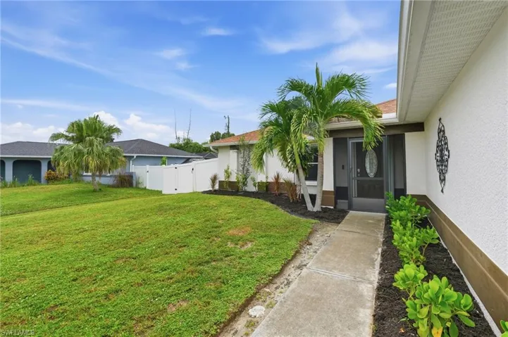 Front entry with a screened door, mature palm trees, landscaped garden beds, and a concrete walkway