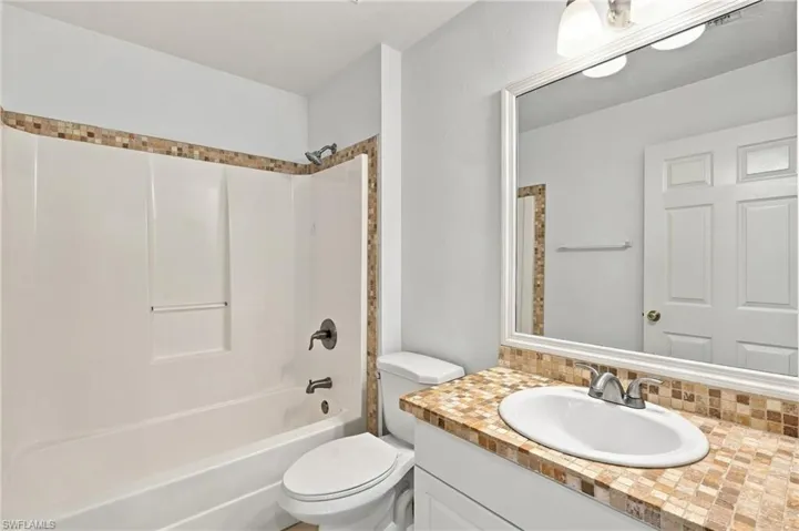 White bathtub with bronze-finish fixtures, a mosaic tile accent, and a coordinating mosaic tile vanity countertop with an integrated sink