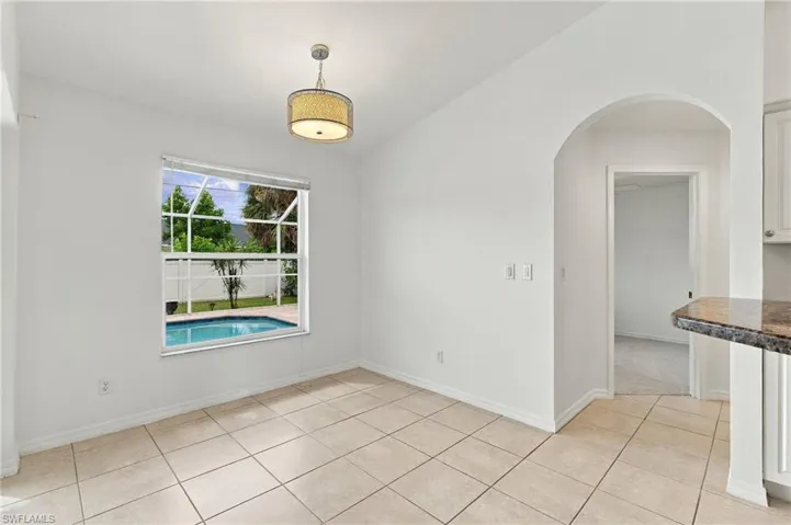 Travertine-style tile flooring, decorative ceiling fixture, arched doorway, and built-in counter with stone-finish surface