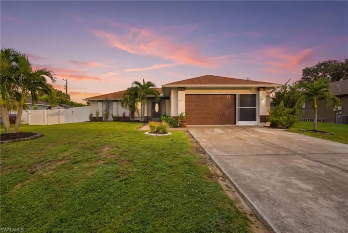 Single-story residence featuring a two-car garage, concrete driveway, and mature palm trees