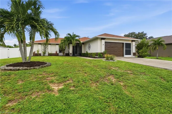 Exterior featuring a concrete driveway, a brown garage door, a white privacy fence, mature palm trees, and manicured landscaping