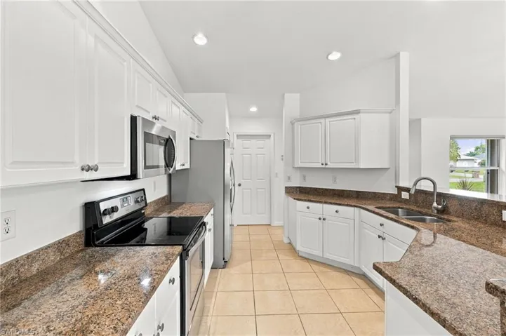 White cabinetry with panel doors, granite countertops, stainless steel appliances, ceramic tile flooring, and vaulted ceiling