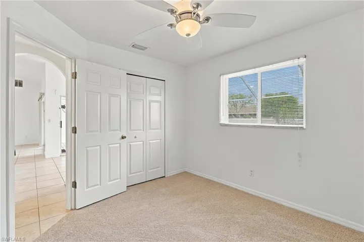 Neutral carpet flooring, bi-fold closet doors, ceiling fan with integrated lighting, and window with horizontal blinds