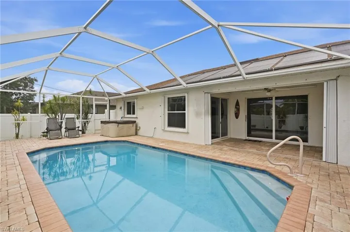 Screened swimming pool enclosure with a paved deck, direct patio access, and integrated hot tub