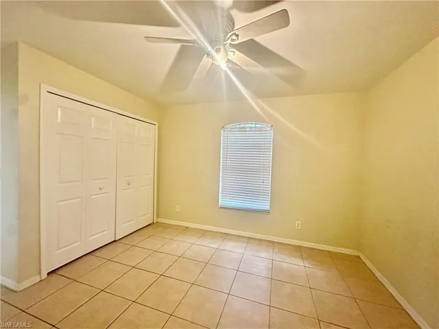 Unfurnished bedroom featuring light tile patterned floors, a closet, a ceiling fan, and baseboards