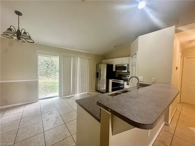 Kitchen featuring light tile patterned floors, a peninsula, a sink, white cabinetry, and appliances with stainless steel finishes