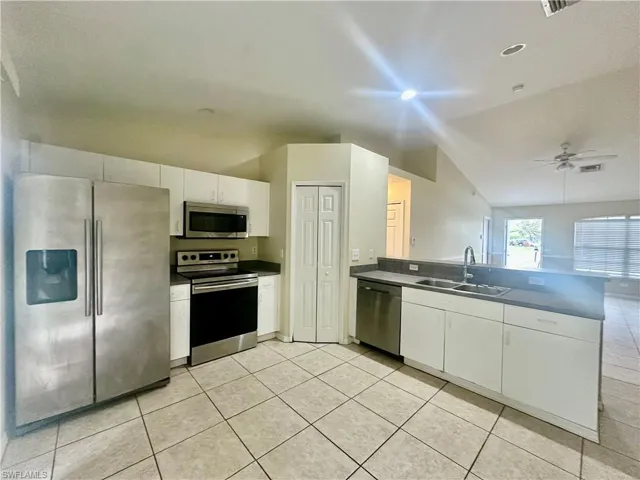 Kitchen featuring light tile patterned floors, dark countertops, appliances with stainless steel finishes, a peninsula, and a sink