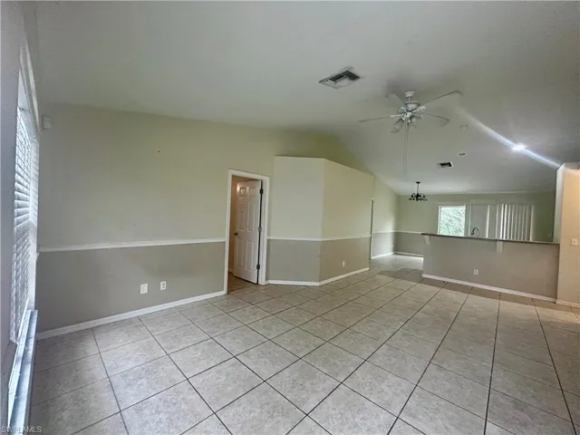 Spare room featuring light tile patterned floors, visible vents, and ceiling fan with notable chandelier
