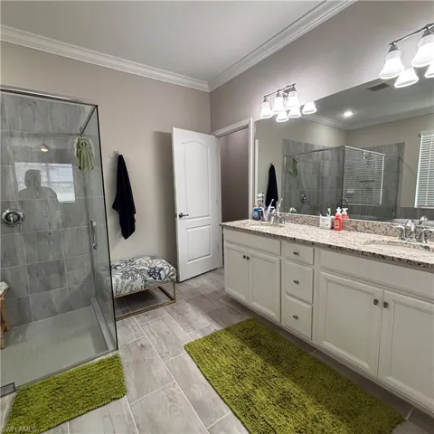 Full bath with double vanity, a shower stall, and crown molding