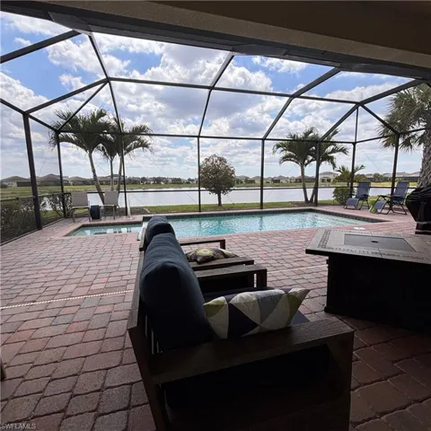 Outdoor pool featuring a sunroom, a patio area, a water view, and glass enclosure