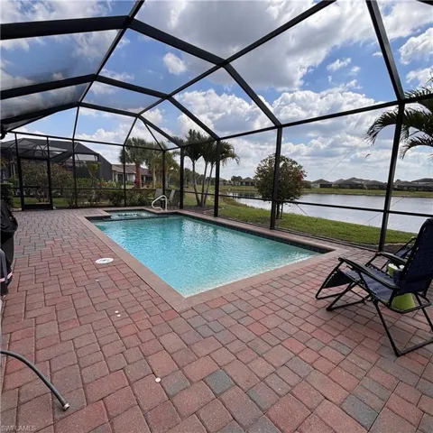 Relaxing pool / spa featuring a sunroom, glass enclosure, a patio area, and a water view