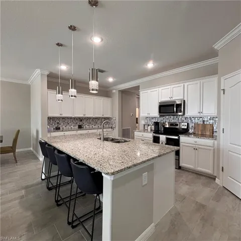 Kitchen with stainless steel appliances, backsplash, white cabinets, a large island with sink, and ornamental molding