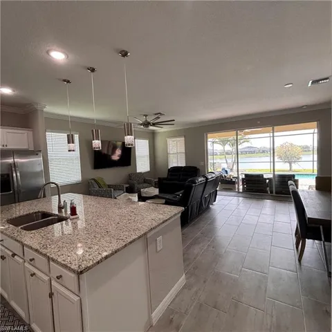 Kitchen with open floor plan, a center island with sink, stainless steel fridge with ice dispenser, white cabinets, and ceiling fan