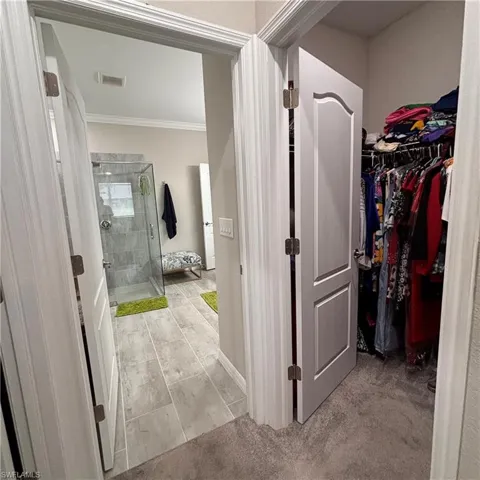Full bathroom featuring a shower stall, a spacious closet, crown molding, and light tile patterned floors