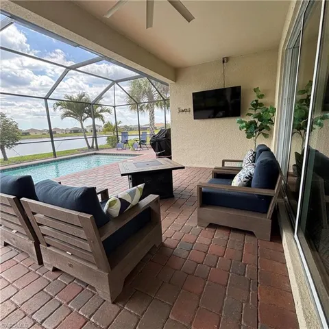 View of patio / terrace with glass enclosure, an outdoor pool, a sunroom, an outdoor living space with a fire pit, and a water view