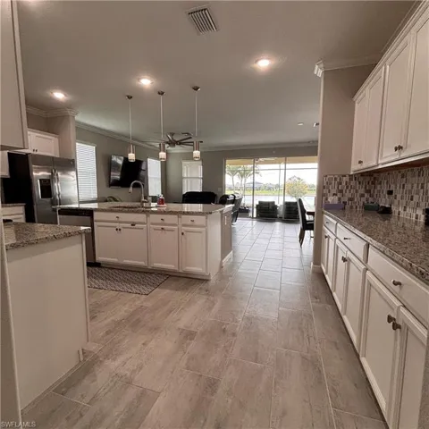 Kitchen with open floor plan, ornamental molding, stainless steel appliances, hanging light fixtures, and white cabinets