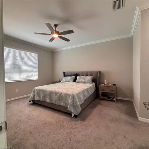 Carpeted bedroom with ceiling fan and ornamental molding