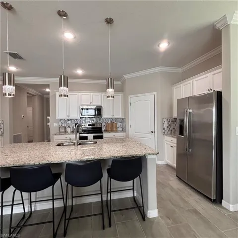 Kitchen with tasteful backsplash, stainless steel appliances, a kitchen bar, white cabinetry, and a large island