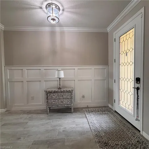 Entryway with crown molding, a decorative wall, wainscoting, and a textured ceiling