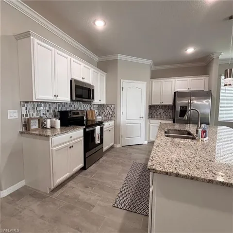 Kitchen featuring white cabinetry, stainless steel appliances, light stone countertops, crown molding, and decorative backsplash